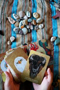 Hands holding animal spirit cards with runes on a woven textile surface.